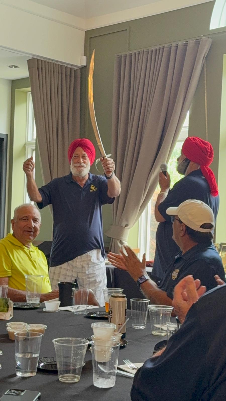 A golfer in a red ceremonial turban raising the curved stainless-steel kirpan aloft in celebration
